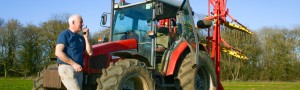 Farmer in the field on a a radio stood by his tractor