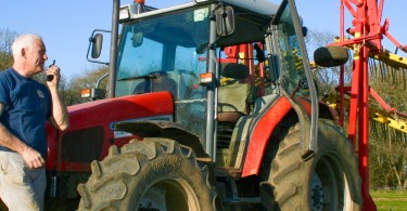 Farmer in the field on a a radio stood by his tractor